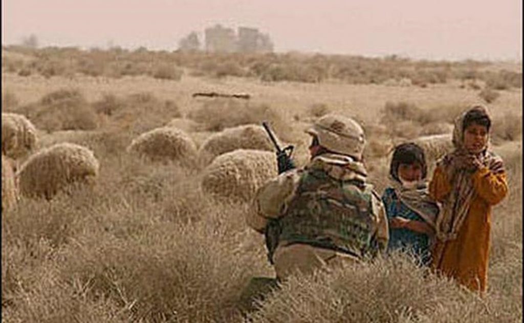 In a gesture of compassion, Bobby Towery in a 2003 photo kneels by two young Iraqi girls who were herding their family’s sheep. Towery and his soldiers routed their convoy around the herd.